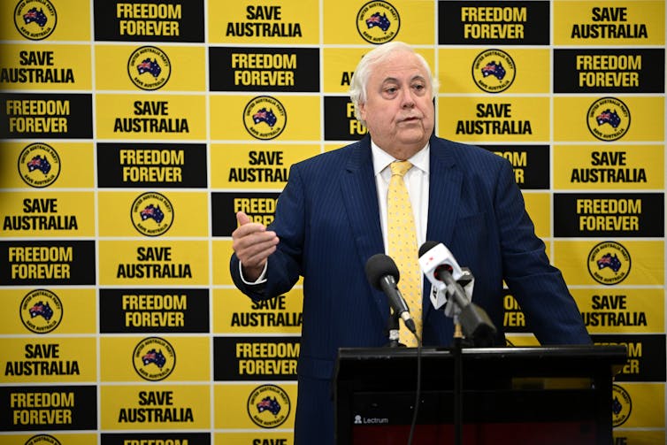 Businessman and United Australia Party founder Clive Palmer standing in front of a yellow and black political banner.