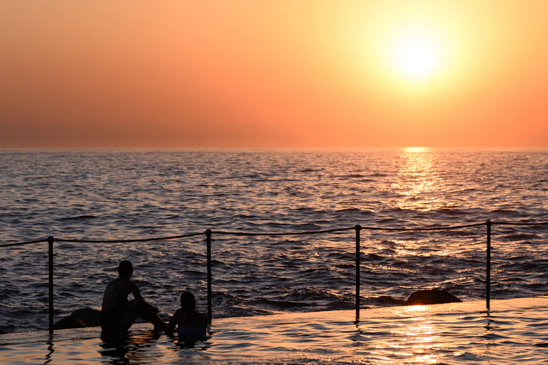 sun sets over ocean, two people in silhouette