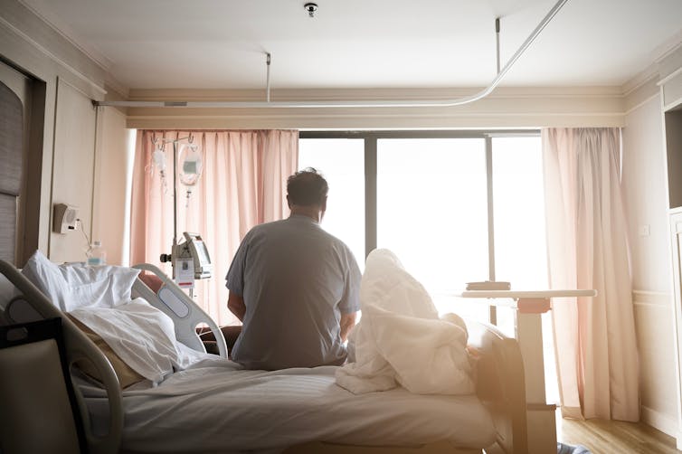 A man sitting up in a hospital bed looking out the window.
