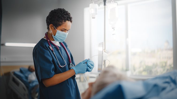 A nurse wearing blue scrubs, a mask and gloves.
