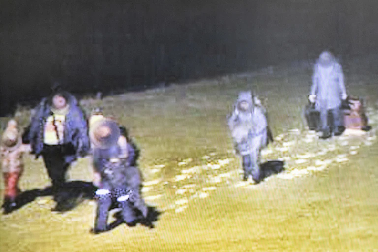 A blurry screengrab from an RCMP video shows people crossing a border at night dressed in winter clothing and pulling suitcases.