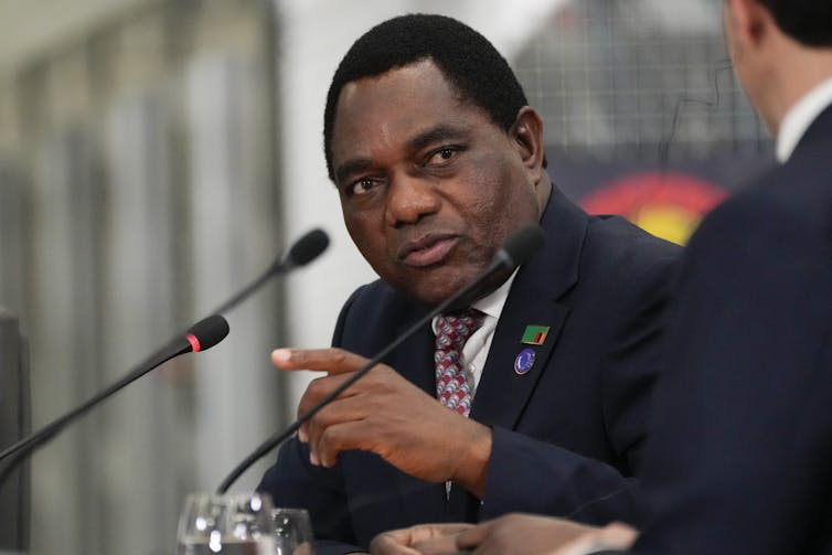 A black man gestures as he speaks to the microphone.