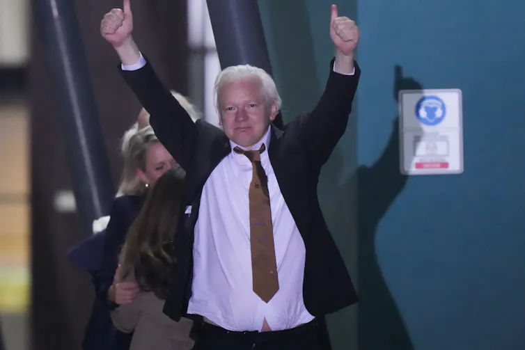 A man with white hair raises his arms in a celebratory gesture.