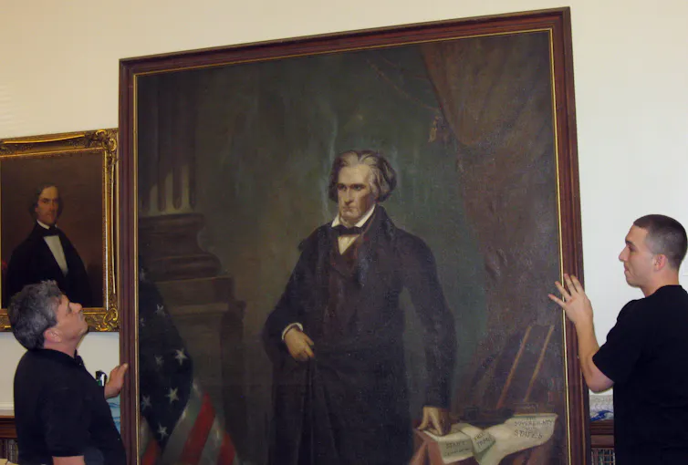Workers take down a painting of a man.