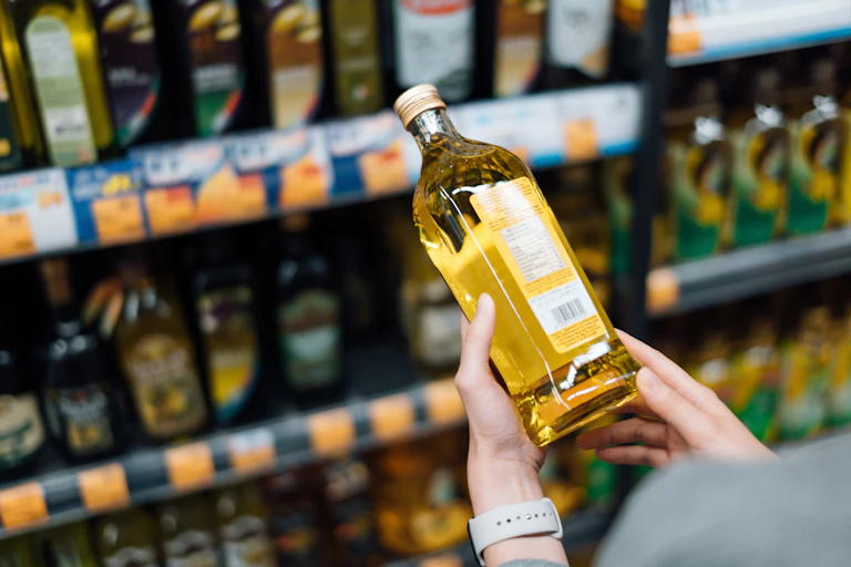 A white person's hands holding a glass bottle of cooking oil