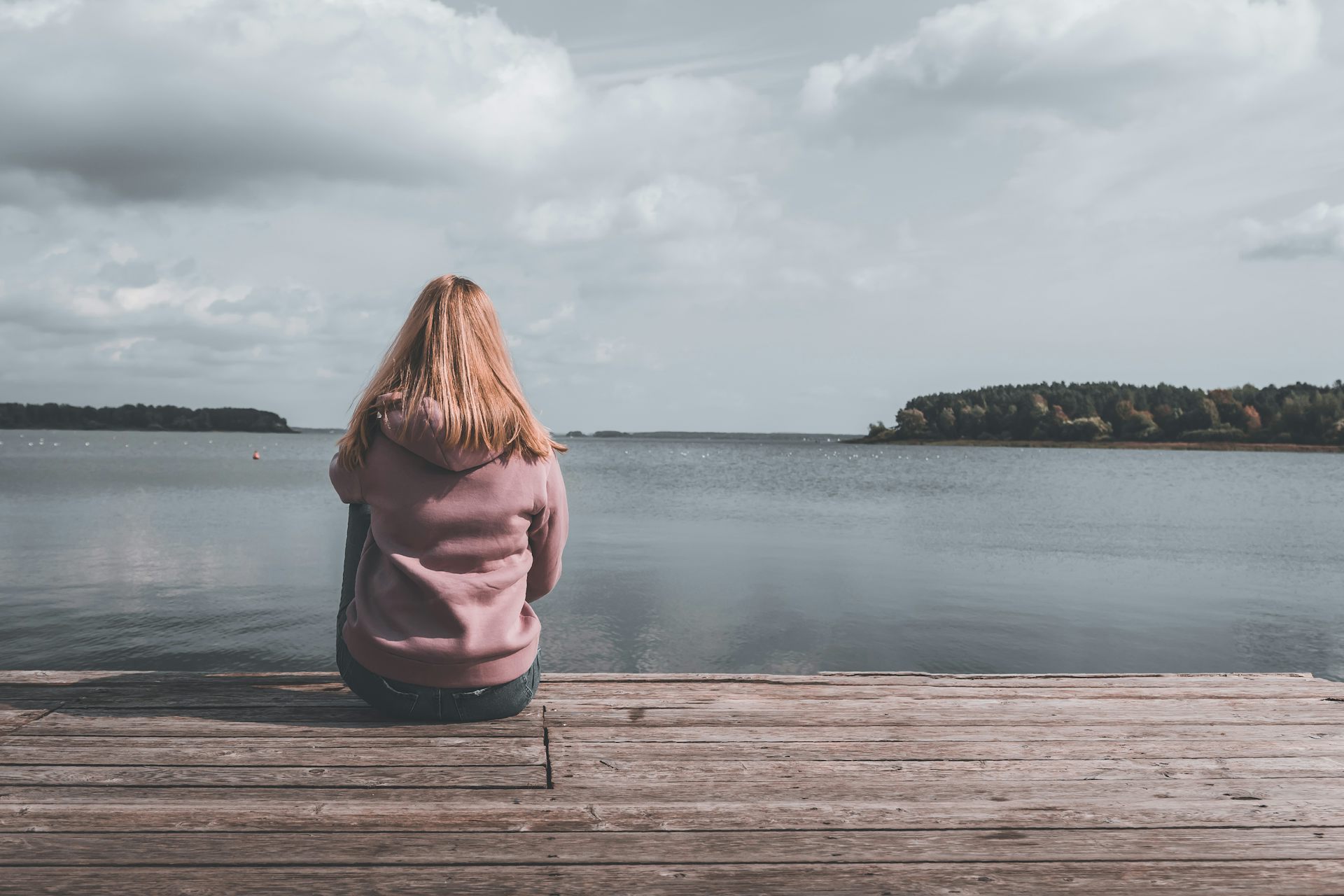 Une fille assise sur un quai regarde un lac devant elle
