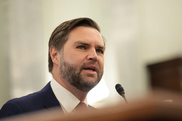 A man in a white shirt and a dark suit is speaking at the lectern.