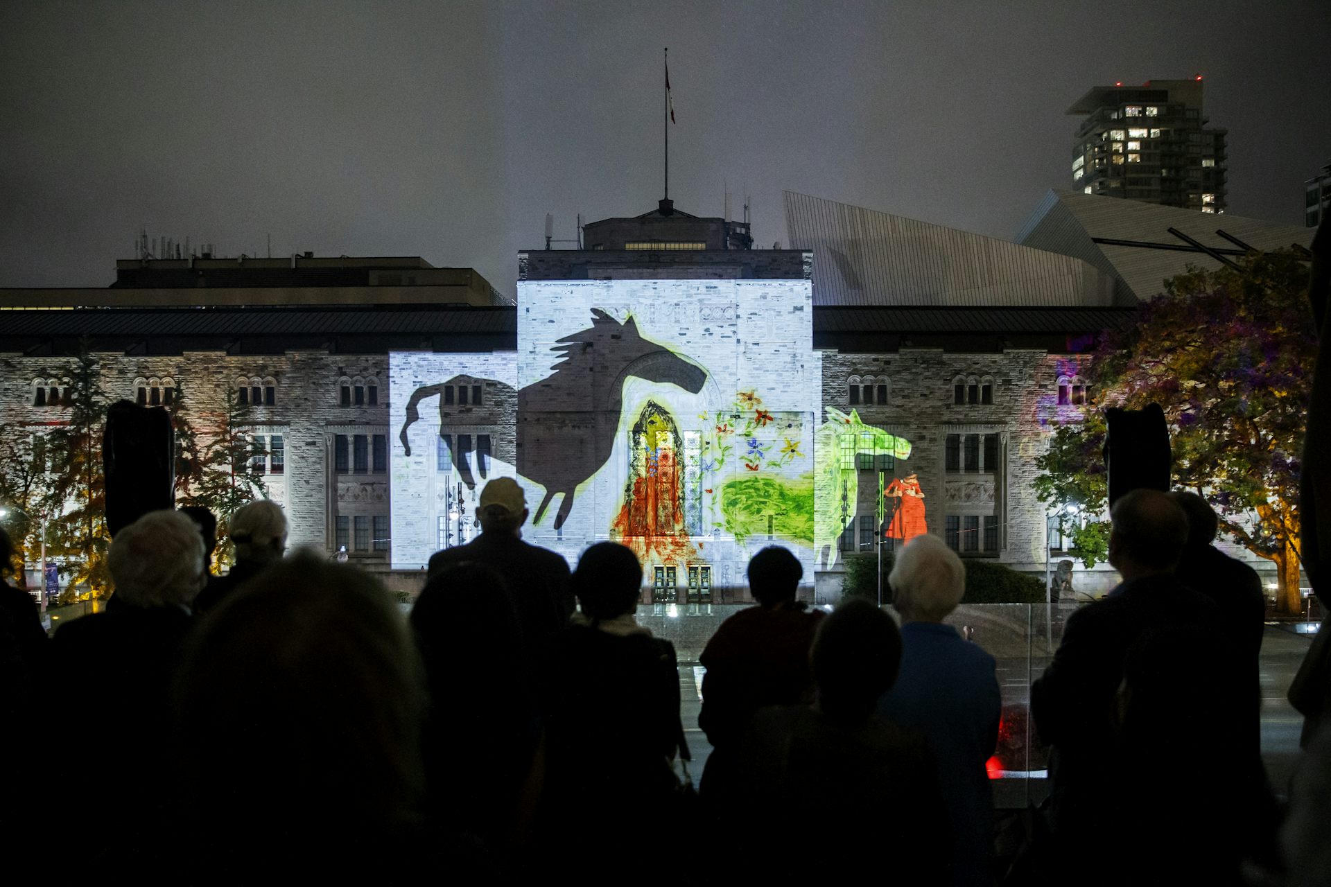 Images of horses seen projected on a building with silhouetted figures.