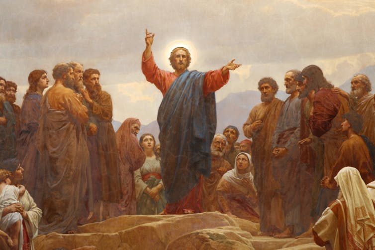 A painting of Jesus, with a halo around his head, surrounded by followers, his hands raised.