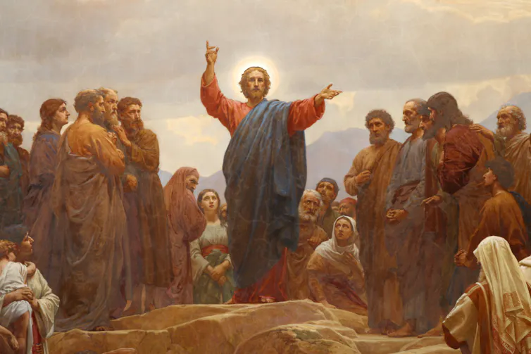 A painting of Jesus, with a halo around his head, surrounded by followers, his hands raised.