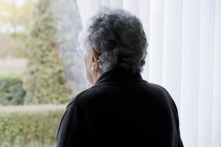 Elderly woman looks out of her window