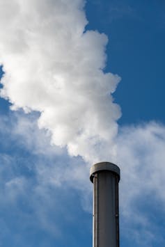 Close up of dense white smoke coming out of an industrial factory chimney against a blue sky background.