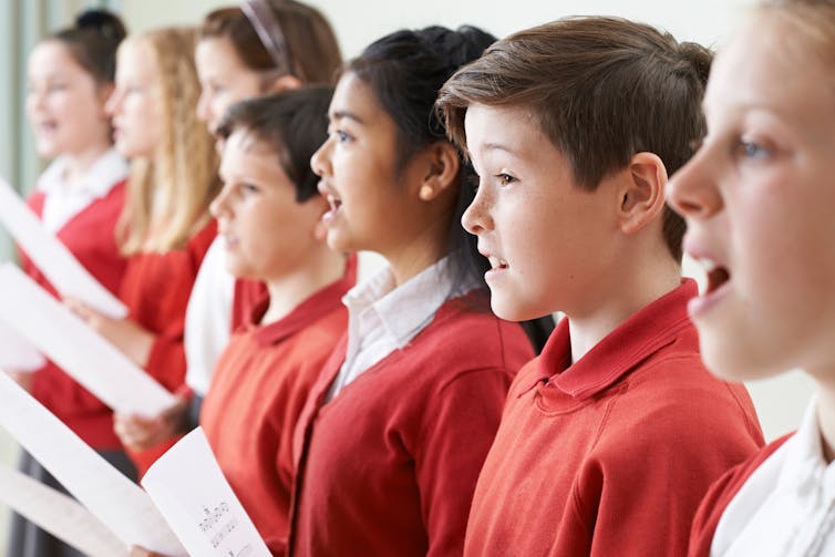 A row of students singing together, holding sheets of paper.