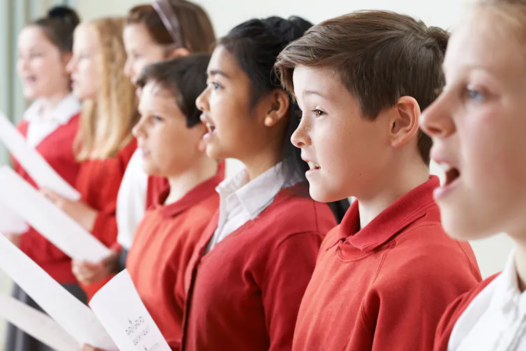 A row of students singing together, holding sheets of paper.