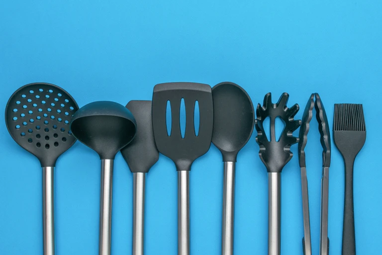 Row of black plastic kitchen utensils lined up against blue background