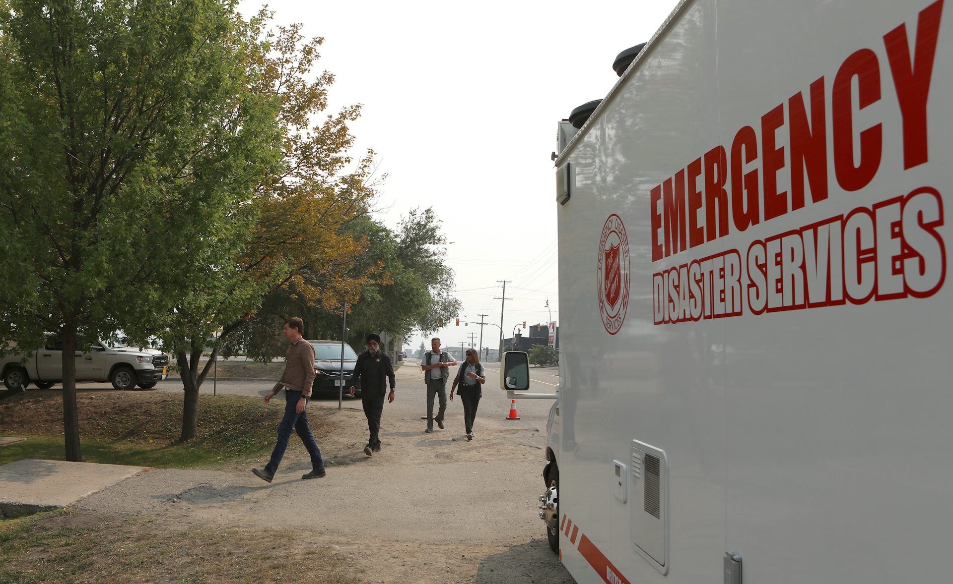 A large white vehicle with Emergency Disaster Services in red letters on the side in the foreground, and people walking in the background