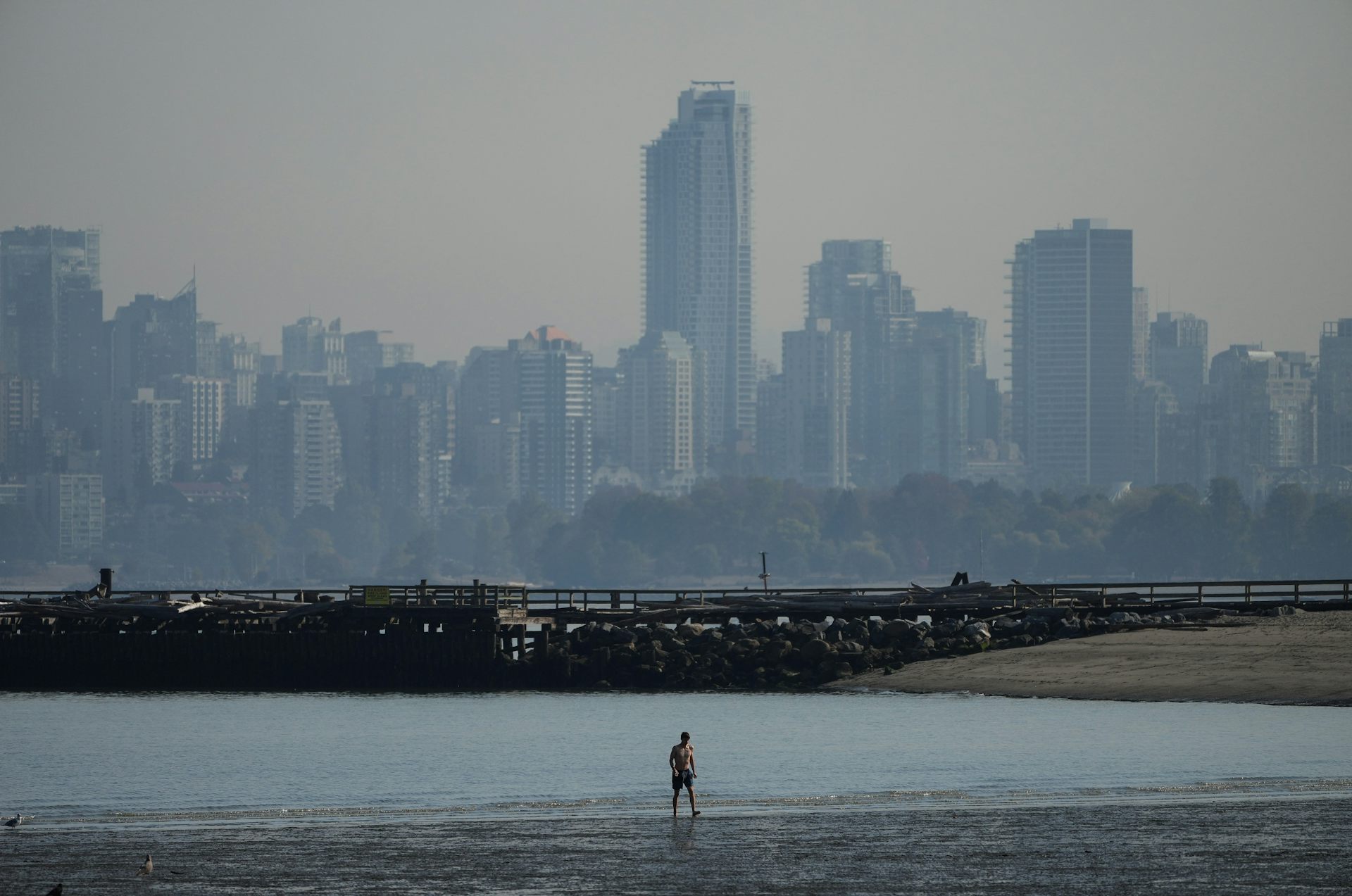 Esquema de la ciudad en el humo del humo en el fondo, y el hombre que camina por la playa en primer plano