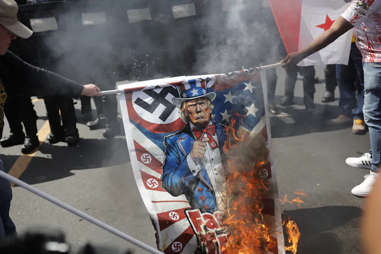 A US flag festooned with swastikas and with a picture of Donald Trump is burned by protesters in Panama City.