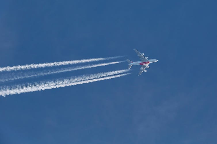 An aeroplane in the upper atmosphere with white contrails.