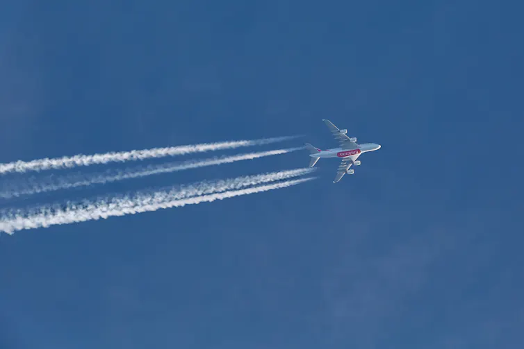 An aeroplane in the upper atmosphere with white contrails.