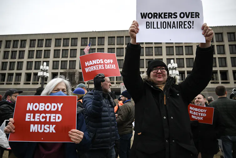 People hold up signs saying 'Nobody elected Musk,' 'Hands off workers data' and 'Workers over billionaires.'