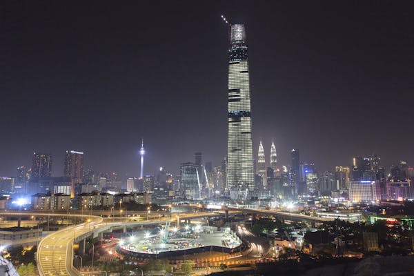 A tower is seen lit up against a city at night.