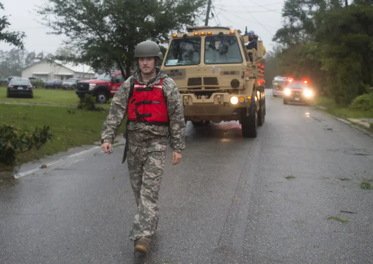 A National Guard member walks in front of search and rescue vehicles.