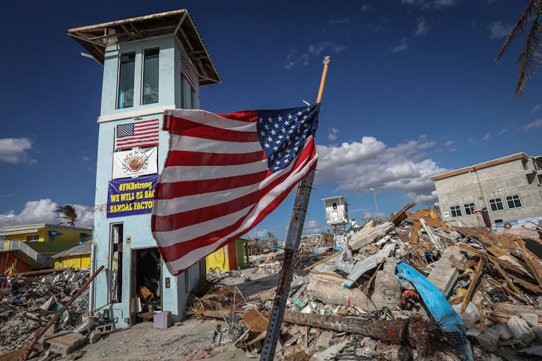 A flag stands in front of rubble and parts of buildings.