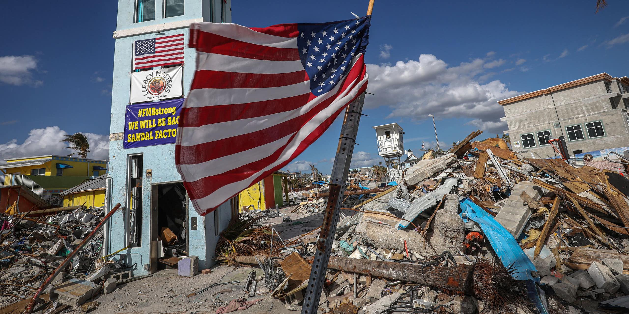 A flag stands in front of rubble and parts of buildings.