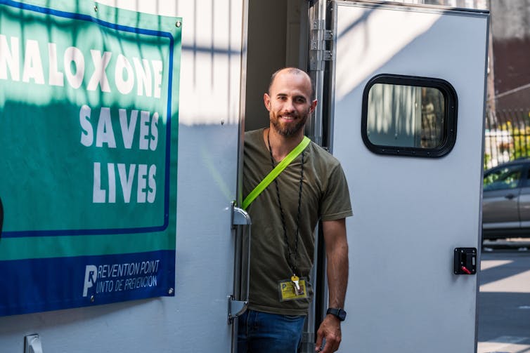 Man stands on steps of white van with sign on its outside that says Naloxone Saves Lives
