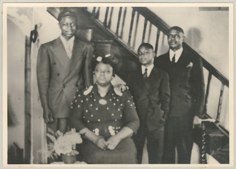 A black-and-white photo of a family, with a woman seated in the center and three Black men standing behind her.