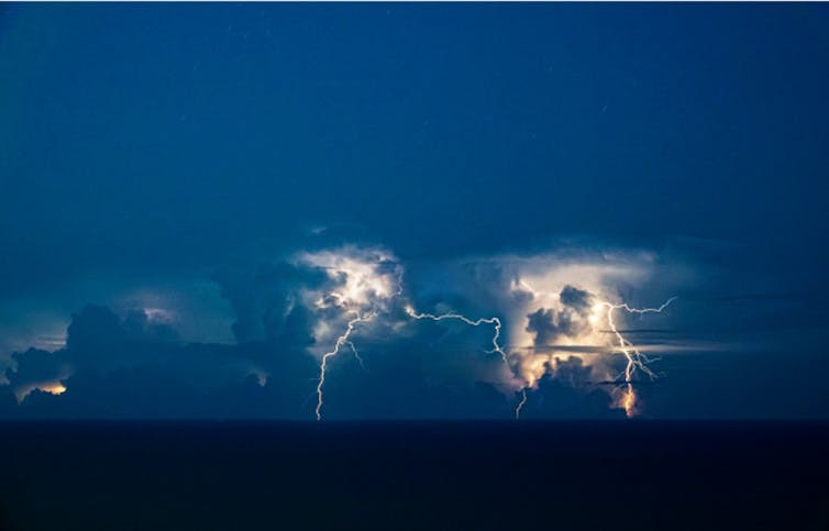 Lightning in clouds, with bolts going to the ocean surface below.