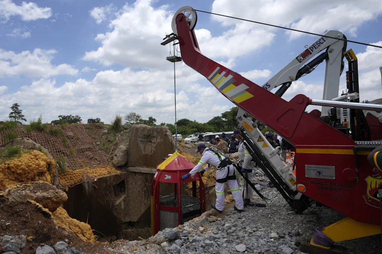 Two people lower a cage from a crane down into a vertical mine shaft