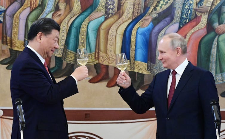 Two men in suits hold wine glasses.