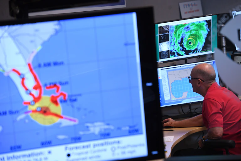 A man sits in front of a bank of computer screens showing hurricane storm surge warnings, a map and the hurricane radar image.