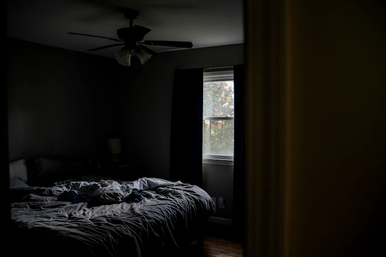 Uma cama desfeita em um quarto escuro.