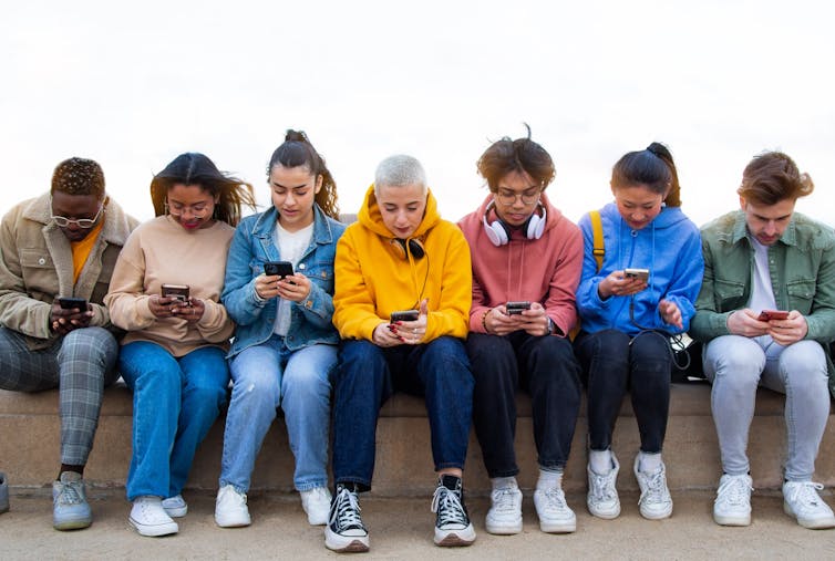 a group of young people sitting in a row each looking at their phones