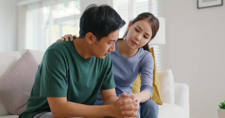 A woman comforts a man as they sit on a couch