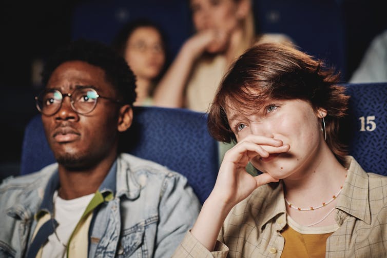 A sad man and woman watching a movie.