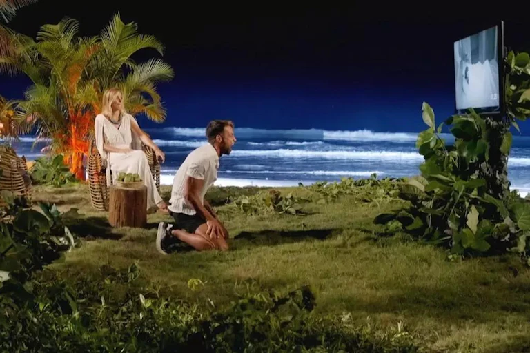 Un hombre al lado de una playa arrodillado viendo un vídeo.