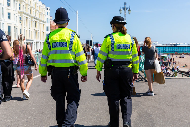 View from behind of two police officers in high vis jackets walking along a busy street in Brighton