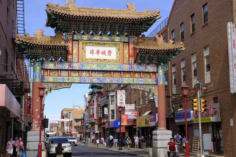 A colorful and elaborate Chinese arch stretches across a street with many stores