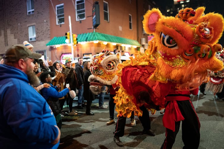 People wear elaborate orange dragon costumes as bystanders on street watch and take photos