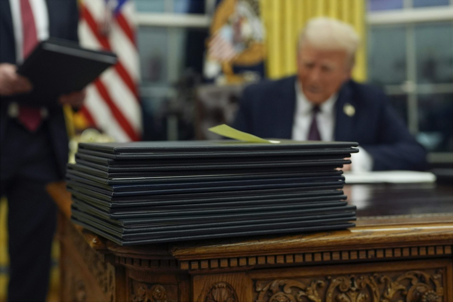 A man in a dark suit out of focus behind a pile of folders