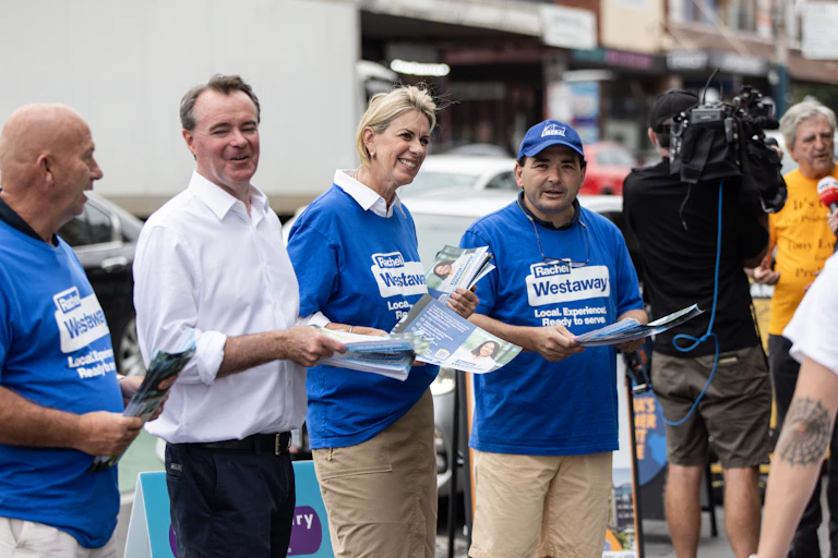 3 people wearing blue Liberal party teshirts and one man in a white shirt handing out how to vote cards