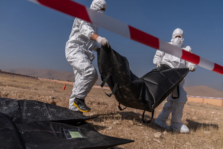 Two people in hazmat suits carry a body bag.