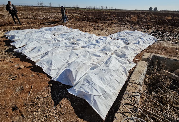 White sheets cover bodies on a dirt floor.