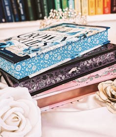A pile of three hardback books with floral pages, on a table with roses and a tiara