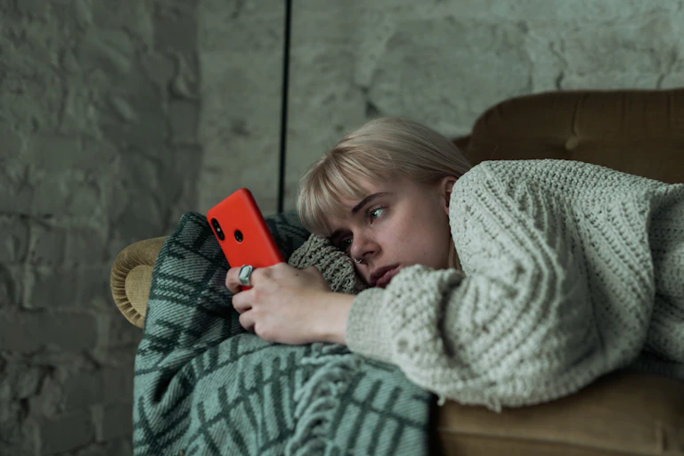 A young woman lying on a couch looking at her phone.