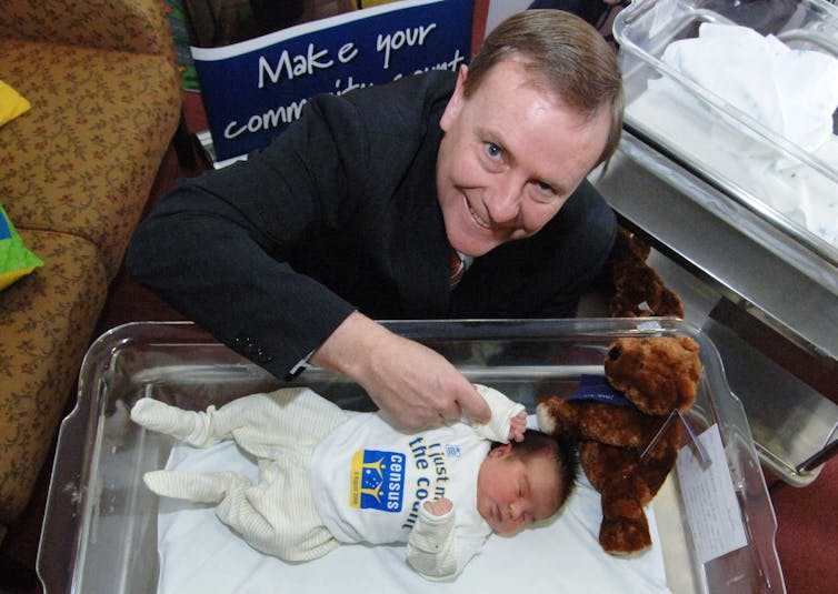 A man in a suit smiles above a sleeping newborn baby